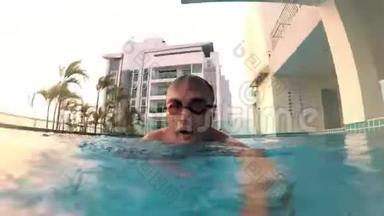 在游泳池里戴着橙色眼镜的活泼的年轻人。 假期暑期时间.. 操作摄像机